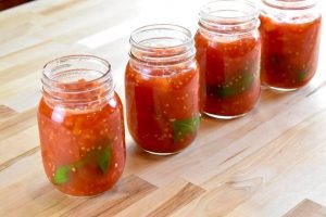 4 mason jars full of diced tomatoes and a basil leaf